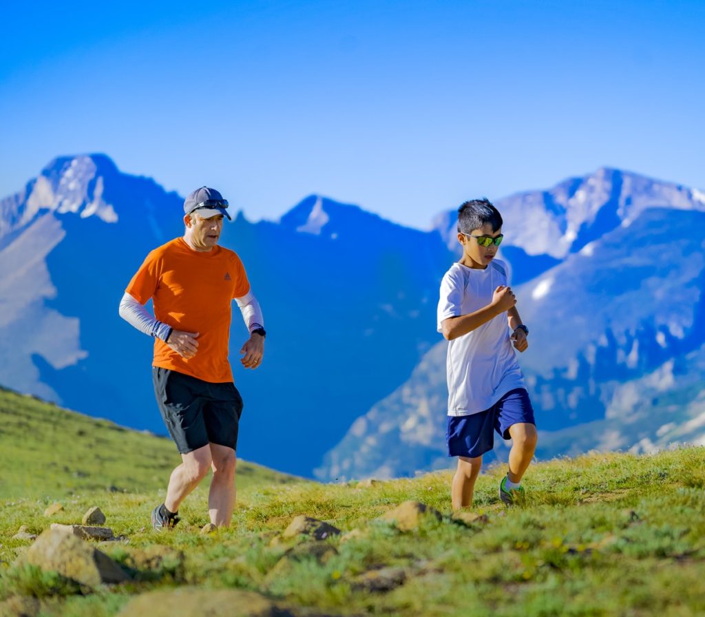 man and boy running on green grass field at daytime